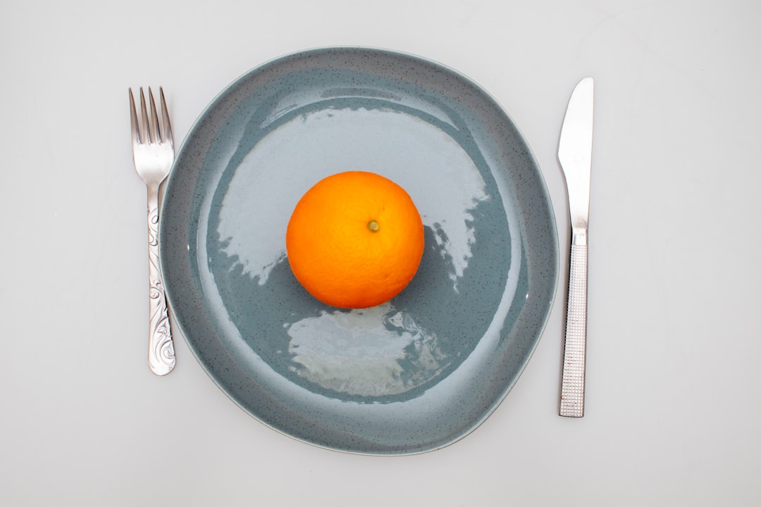 A plate with an orange and a fork and knife